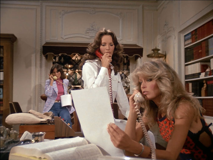 All three angels talking on phones, sitting various distances from the camera