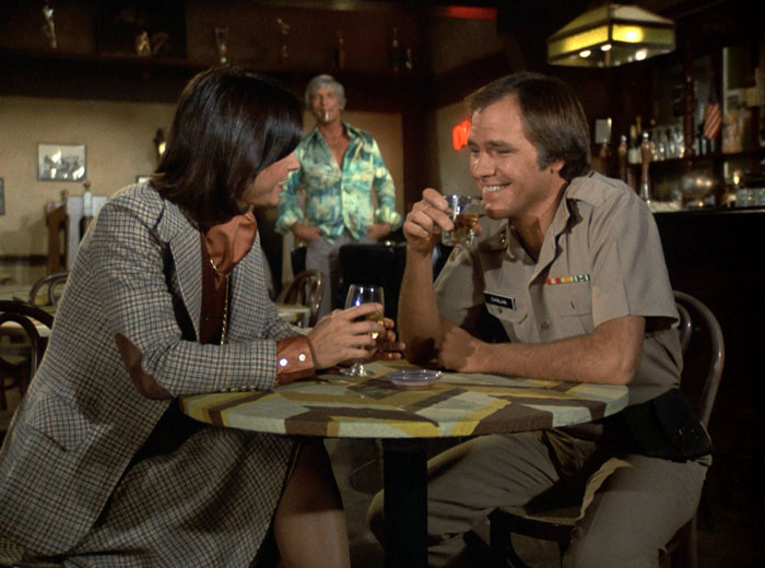 Sabrina (Kate Jackson) and Conlan (Robert Pine) have a drink and a laugh while Billings (L.Q. Jones) looks on in the background in a bright polyester shirt.
