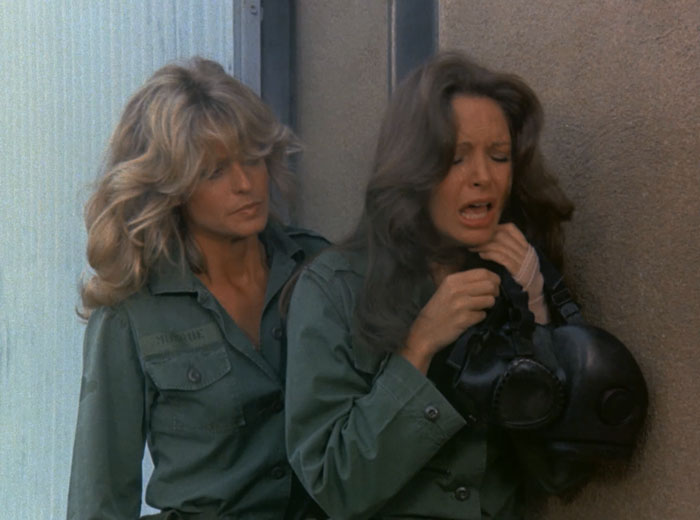 Jill (Farrah Fawcett) checks on a choking Kelly (Jaclyn Smith) who is holding her broken gas mask.