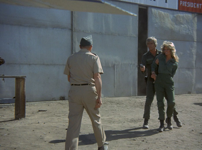 Billings (L.Q. Jones) holds Jill hostage and points a gun at an approaching soldier.