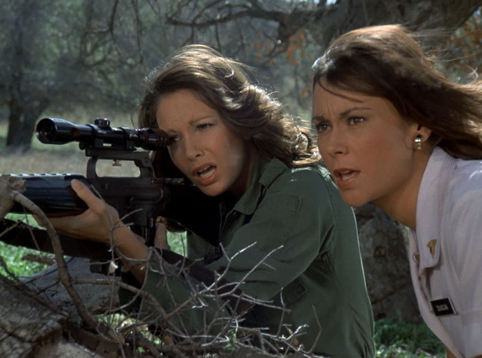 Kelly (Jaclyn Smith) in Army fatigues, looking through the scope of a sniper rifle while Sabrina (Kate Jackson) looks on in her nurse uniform
